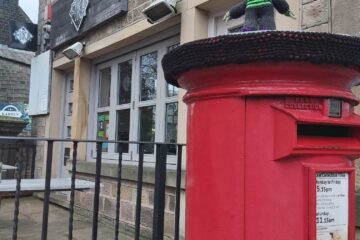 A post box in Uppermill with a knitted hat.