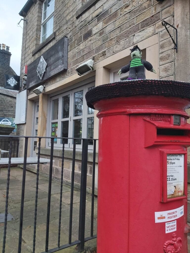 Yarn bombing in Uppermill. Pic of a knitted hat on a post box put up for Eleanor, really.